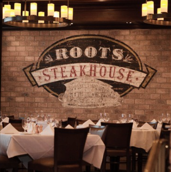 Roots Steakhouse dining room with signage plaque on a brick wall and wine-bottle shelving